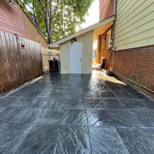 Lumen Landscaping | Guelph Charcoal stamped concrete in a square slate pattern, sealed, running along a side yard to a shed