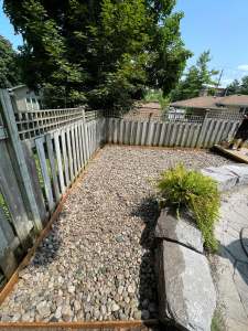 Lumen Landscaping | Runoff From the Neighbour’s Yard River rock bed with large armour stone boulders and an ornamental grass along a wood fence