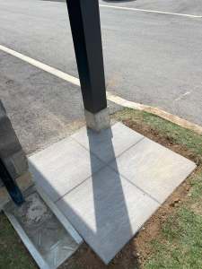 Lumen Landscaping | Cracked Concrete Steps and Porch Small broom finish concrete pad with tooled joints around a black post beside a road