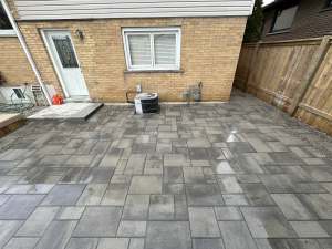 Lumen Landscaping | Interlock Patios Grey large format interlock patio behind a yellow brick house with a wood privacy fence, Hamilton Mountain