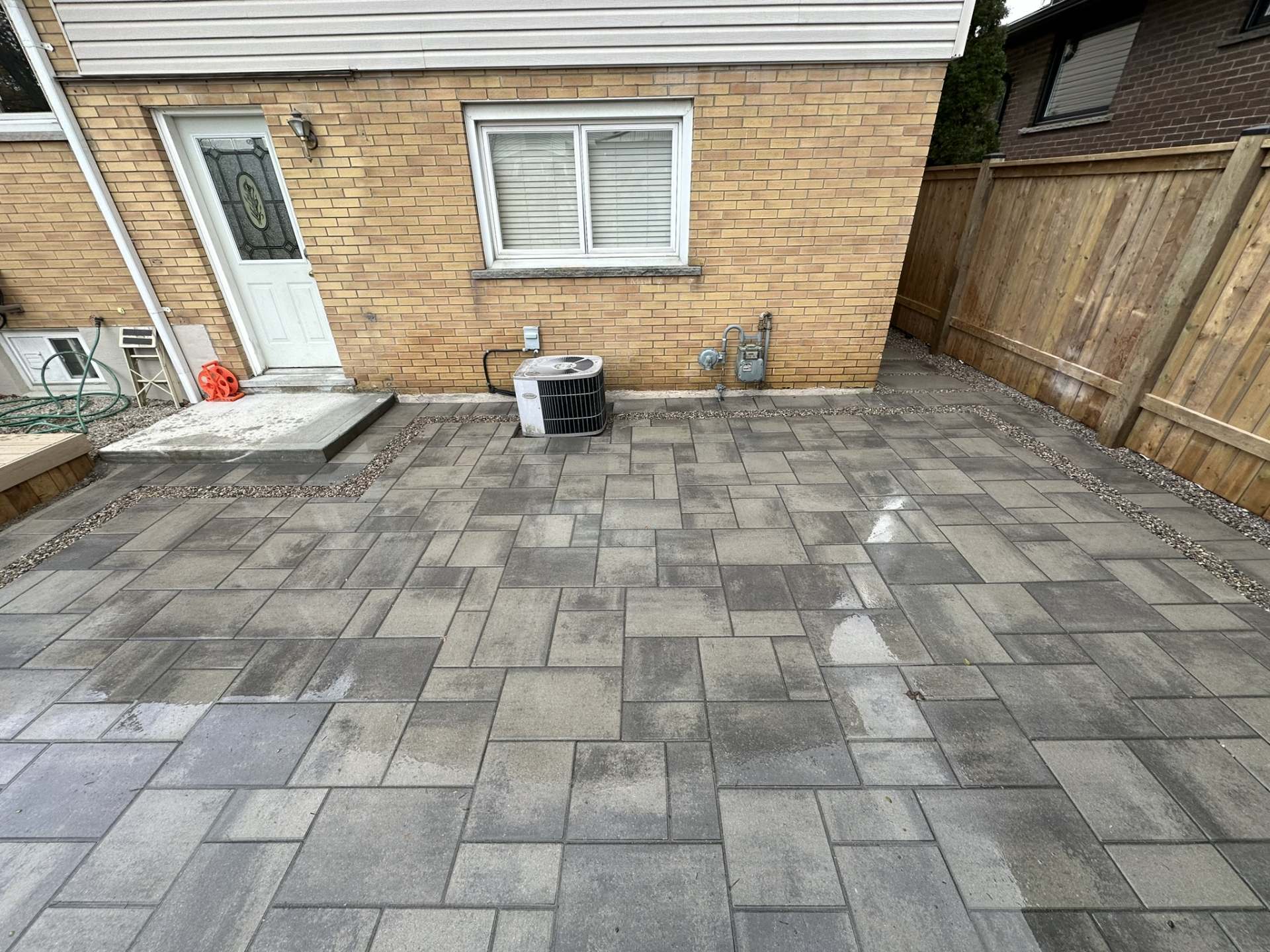 Lumen Landscaping | Hamilton Large format grey interlock patio behind a yellow brick home on Hamilton Mountain, built by Lumen Landscaping