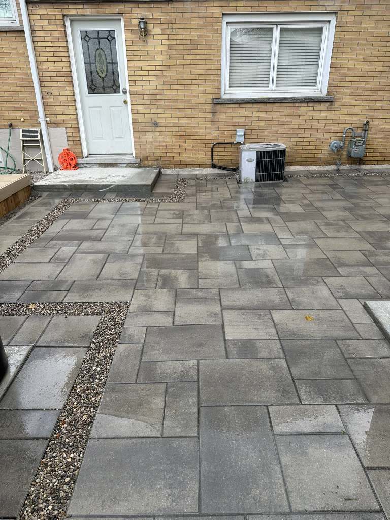 Lumen Landscaping | Weeping Tile for Homeowners Grey interlock patio at a back door with a pea gravel inlay strip, yellow brick house, Hamilton Mountain