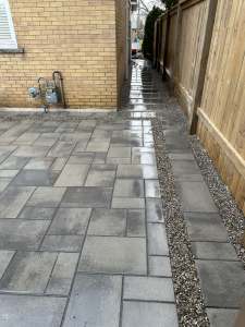 Lumen Landscaping | Muddy Side Yard Grey interlock walkway running down a side yard beside a wood fence with a pea gravel strip, Hamilton Mountain