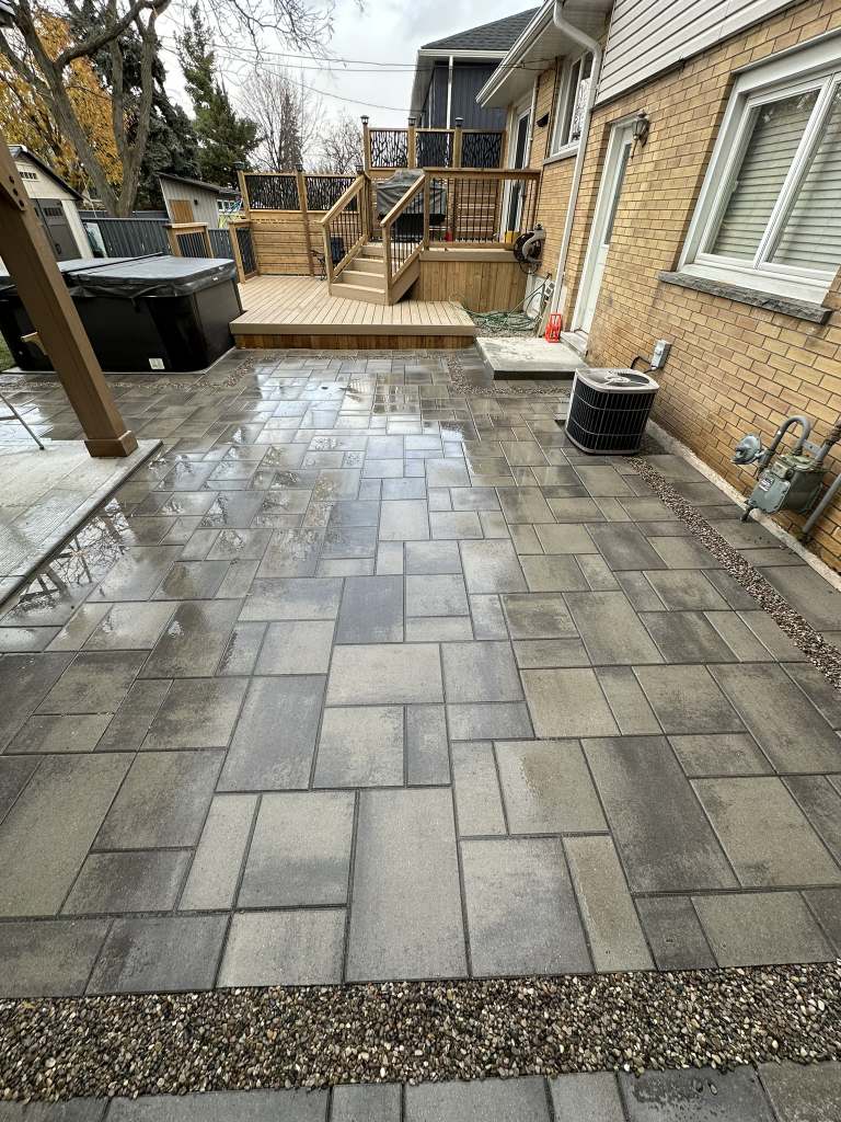 Lumen Landscaping | Wet Look or Natural? Choosing an Interlock Sealer Grey interlock patio beside a raised wood deck behind a brick house, Hamilton Mountain
