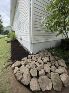 Lumen Landscaping | Garden Bed Cleanup, Mulch and Edging Side garden bed cleared to fresh soil with rough stones at the house corner in Mount Hope