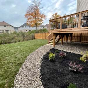 Lumen Landscaping | Water Draining Toward the House New sod lawn, river rock strip and black mulch bed with shrubs beside a raised wood deck