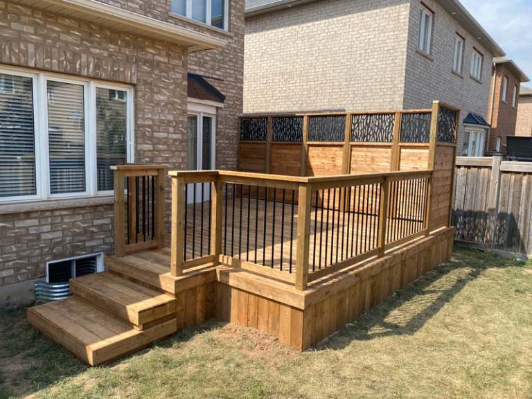 Lumen Landscaping | Home Landscaping Pressure-treated wood deck with black balusters, wide stairs and a privacy screen