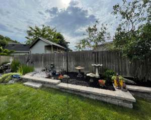 Lumen Landscaping | Ancaster Raised garden bed with a stone block wall and caps, mulch and ornaments in a fenced backyard