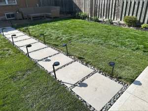 Lumen Landscaping | Water Pooling in the Yard Large slab stepping stones set in river rock with path lights across a new backyard lawn