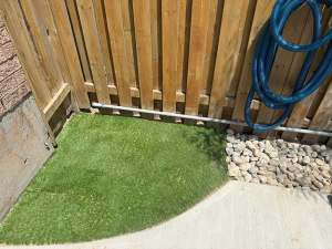 Lumen Landscaping | Weeds in River Rock Small curved patch of artificial turf beside a river rock strip and a concrete walkway