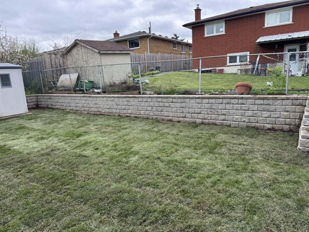 Lumen Landscaping | Turning a Sloped Escarpment Yard Into Usable Space Tan block retaining wall across the back of a yard with freshly laid sod in front