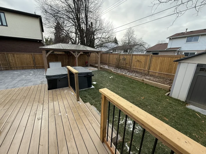 Wood deck with a pavilion and interlock patio Wood deck overlooking a pavilion over a hot tub, an interlock patio and a fenced lawn