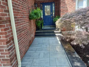 Lumen Landscaping | Cracked Concrete Steps and Porch Front walkway in large grey slabs with a dark border leading to black steps and a blue door