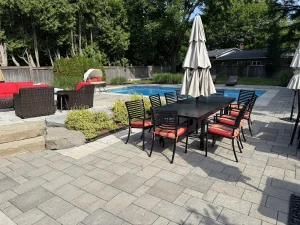 Lumen Landscaping | Sinking Interlock Patio Grey slab pool patio with a dining set and natural stone steps beside an inground pool