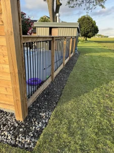 Lumen Landscaping | Yard Drainage Wood fence with black metal picket panels and a river rock strip along the base